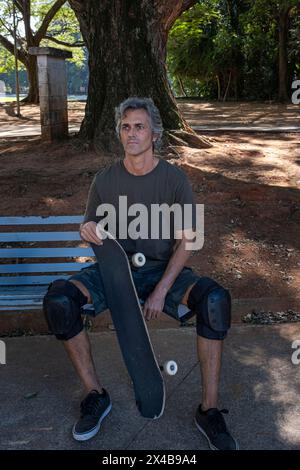 Brasilianischer Skateboarder, der über 50 Jahre alt ist und sich auf einer Bank in einem Quadrat entspannt 2. Stockfoto