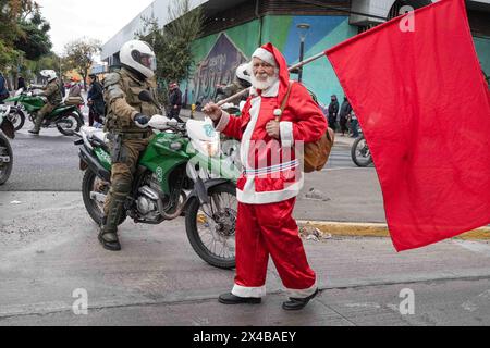 Santiago, Metropolregion, Chile. Mai 2024. Ein Mann, der als Weihnachtsmann gekleidet ist, läuft vor einem Polizeibeamten von Carabineros während des Internationalen Arbeitertags in Santiago, Chile. Mai 2024. (Kreditbild: © Joshua Arguello/ZUMA Press Wire) NUR REDAKTIONELLE VERWENDUNG! Nicht für kommerzielle ZWECKE! Stockfoto