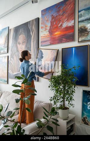 Frau hängt ein Bild an die Wand. Malerin, die die Kombination von Malfarben schätzt. Stockfoto