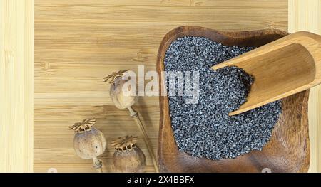 Kleine Holzschale gefüllt mit schwarzen Mohnsamen und getrockneten Mohnköpfen auf rustikalem Holztisch Stockfoto