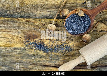 Holzlöffel gefüllt mit schwarzen Mohnsamen in der Nähe eines Nudels auf einem rustikalen, verwitterten Holztisch, der eine warme und nostalgische Szene setzt Stockfoto