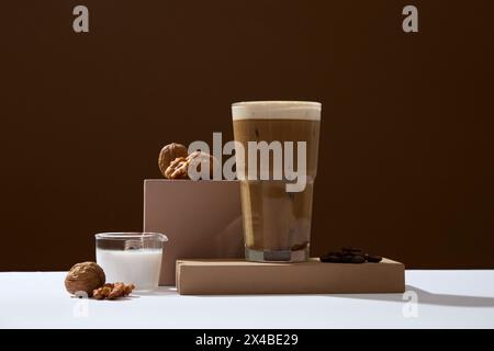 Auf einem dunkelbraunen Hintergrund ist eine Tasse Kaffee mit reichhaltiger Creme mit Walnüssen, gerösteten Kaffeebohnen und Milch dekoriert. Werbefoto. Kaffee ist schon Stockfoto