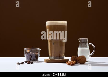 Werbeszene für beliebte Getränkeprodukte mit Kaffeezutat. Eine köstliche Tasse Kaffee mit Bohnen, Walnüssen und Milch auf braunem Hintergrund. Aktiv Stockfoto