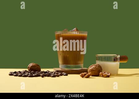 Minimale Szene für die Werbung für ein Getränk mit einer köstlichen Tasse Kaffee, Bohnen, Walnüssen und Milch auf grünem Hintergrund. Koffein in Kaffee hilft bei der Fokussierung Stockfoto