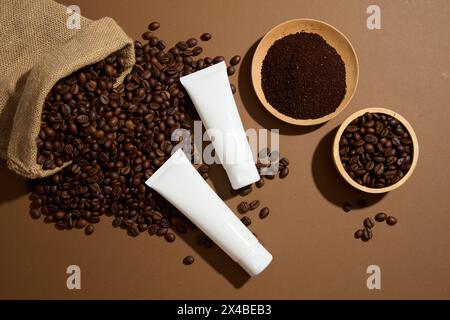 Zwei Kosmetikröhrchen, Behälter Creme oder Maske mit Kaffeeextrakt, dargestellt auf braunem Hintergrund mit natürlicher Zutat. Kaffeebohnen und gemahlen auf Holz Stockfoto