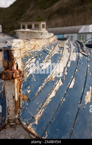 Altes beschädigtes Holzruderboot mit abblätternder Farbe, das auf dem Anleger eines Fischerhafens verlassen wurde. Stockfoto