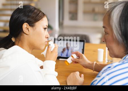 Asiatische Großmutter und birassische Enkelin rufen zu Hause an, eine blühende Nase. Lässig gekleidet, entspannte Momente mit nachdenklichem Ausdruck Stockfoto