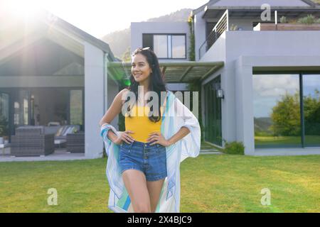 Birassische junge Frau, die draußen vor dem Haus steht. Mit Shorts und einem Handtuch, mit langen dunklen Haaren, an einem sonnigen Tag, unveränderlich Stockfoto