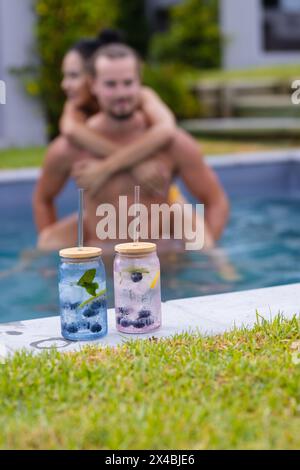 Verschiedene Paare, die sich im Freien im Pool, Getränke in der Nähe, Kopierraum umarmen. Sie hält ihn fest, zeigt hellbraunen Hintergrund und lockiges Haar; er, W Stockfoto