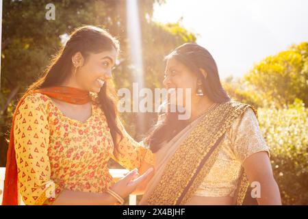 Indische Mutter und Teenager-Tochter teilen sich einen freudigen Moment im Freien. Beide tragen traditionelle Kleidung, eine junge Frau, die ein Smartphone hält, unverändert Stockfoto