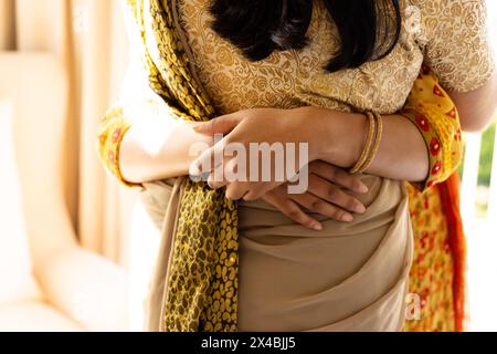 Indische Mutter und Tochter im Teenageralter, umarmt zu Hause, trägt traditionelle Kleidung. Beide zeigen Zuneigung, Mutter hat dunkle Haare und kreiert warme atmos Stockfoto