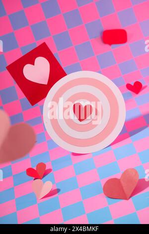 Vorderansicht des niedlichen Bullseye, verziert mit roten Papierherzen und Karte auf rosa und lila kariertem Hintergrund. Minimale Szene für Werbung Stockfoto