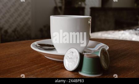 Keramikkkaffeetasse auf einem Holztisch mit ein paar Kaffeekapseln daneben Stockfoto