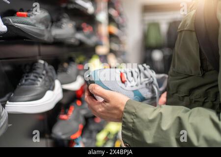 Mann, der Sneakers im Laden kauft, hält ein Paar Schuhe in der Hand. Stockfoto