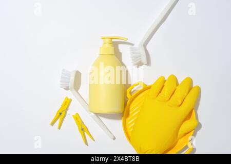 Ein gelber Gummihandschuh auf einer Keramikplatte, eine unbeschriftete Plastikflasche, zwei Wäscheständer und zwei Toilettenbürsten auf weißem Hintergrund. Werbefläche Stockfoto