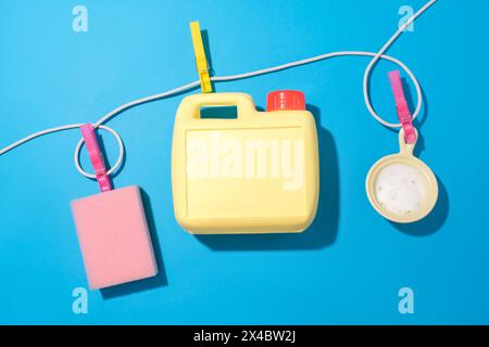 Ein Seil mit drei Wäscheständern hält drei Gegenstände an Ort und Stelle, darunter einen rosafarbenen Schwamm, eine gelbe Flasche Waschmittel und eine kleine Keramikschale auf blauem Rücken Stockfoto