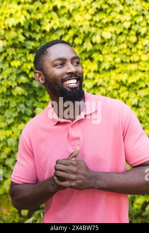 Afroamerikaner mit rosa Hemd, lacht draußen zu Hause. Er hat einen kurzen Bart, kurze schwarze Haare und dunkle Augen, unverfälscht Stockfoto