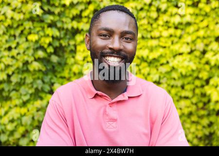 Ein Afroamerikaner in rosa Hemd, der draußen lächelt. Ein rosafarbenes Hemd, kurze schwarze Haare, einen Bart und helle Augen, frische Luft genießen, Stockfoto