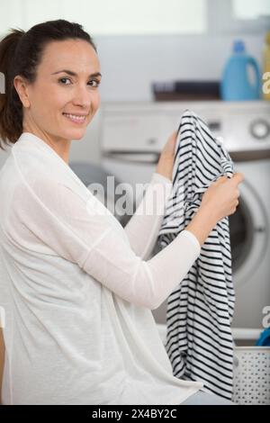 Glückliche Frau mit sauberer Wäsche am Tisch drinnen Stockfoto