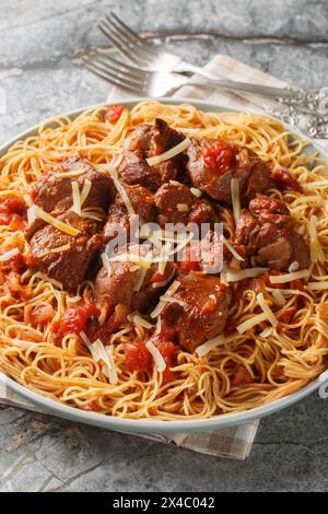 Langsam gedünstetes Rindfleisch in Wein-Tomatensauce serviert mit Spaghetti in Nahaufnahme auf einem Teller auf dem Tisch. Vertikal Stockfoto