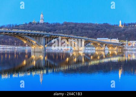 Ukraine, Kiew, Kiew. Metro Bridge über den Dnieper River. Dächer des Klosters der Höhlen (Petschersk Lavra) im Hintergrund. Stockfoto
