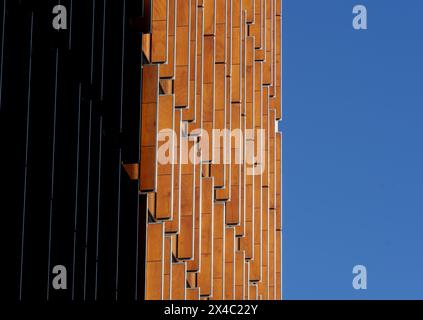 Mosaik aus Formen, Mustern und Farben an der Fassade eines Gebäudes mit orangefarbenen Holzfenstern, einem bläulichen wolkenlosen Himmel und der Hälfte des Gebäudes Stockfoto