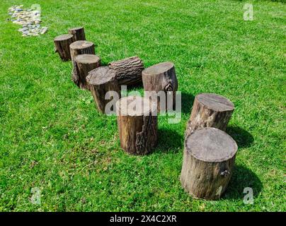 Ein Weg, der barfuß gemacht werden muss: Holzstämme auf einem Rasen, gefolgt von einem abgerundeten Stein. Schöner sonniger Tag. Stockfoto