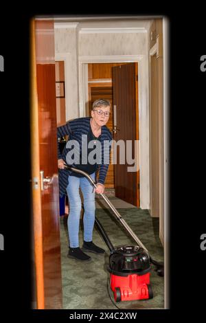 Reife Frau saugt Teppich im Hausflur zu Hause ab. Stockfoto