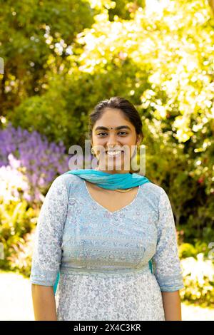 Indische junge Frau in traditioneller Kleidung, lächelnd in die Kamera, Kopierraum. Umgeben von Grün und Blumen, Hand mit ihrem Teenager-Töchter Stockfoto