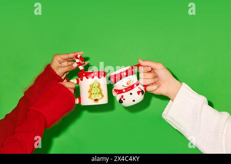 Hände halten Tassen mit Weihnachtsmotiv vor grünem Hintergrund. Heißer Tee, Kakao und heiße Schokolade Stockfoto