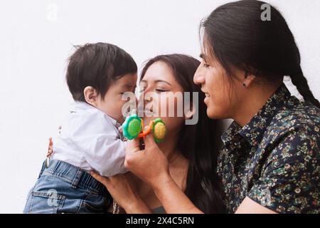 Ein ecuadorianisches Paar, ein Mann mit einem traditionellen Zopf und eine Frau, teilen einen liebevollen Moment mit ihrem Baby und betonen die Einheit der Familie und die kulturelle Tradition Stockfoto