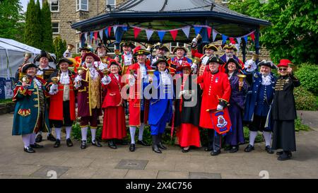 Stadtschreier stehen in großer Gruppe, Lächeln (Pagen und Pagen in bunten geflochtenen Uniformmänteln) - Ilkley Bandstand, West Yorkshire, England, Großbritannien. Stockfoto