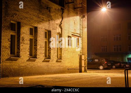 Eine Laterne, die an einem Industriebau befestigt ist und glüht, eine Laterne an einer Hauswand, leichter Nebel, industrielle Atmosphäre Stockfoto