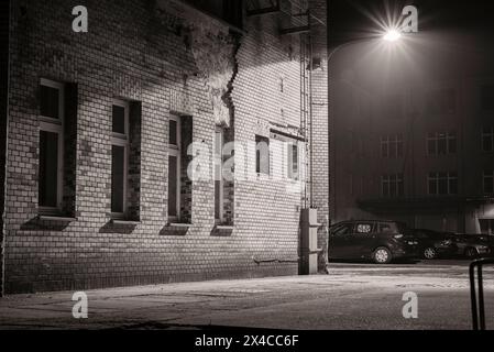 Eine Laterne an einem Industriebau angebracht und glühend, eine Laterne an einer Hauswand, leichter Nebel, industrielle Atmosphäre, Schwarzweißfoto Stockfoto