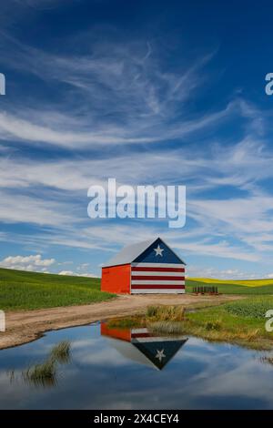 USA, Idaho, Genesee. Scheune in Rot, weiß und Blau und Reflexion in einem kleinen Teich Stockfoto