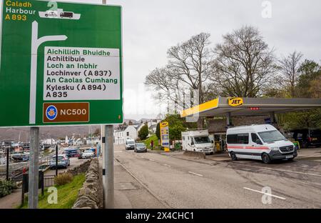 Wegweiser zur NC500 in der schottischen Fischerstadt Ullapool mit einem Wohnmobil an der Jet Tankstelle Stockfoto