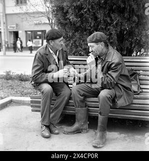 Die Sozialistische Republik Rumänien in den 1970er Jahren Zwei Männer in Arbeitskleidung rauchen und trinken Bier auf einer Bank in der Stadt. Stockfoto