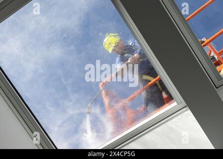Arbeiter auf einem Kirschpflücker, der Dachfenster mit Hochdruckwasserstrahl reinigt. Aufnahmen mit niedrigem Winkel Stockfoto