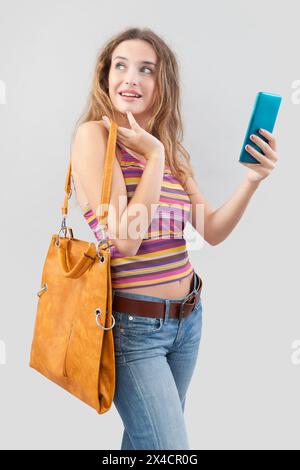 Die lächelnde junge Frau, die eine Vintage-Ledertasche trägt, trägt modische Kleidung, während sie auf einer Internetseite oder einem Online-Shop surft und h verwendet Stockfoto