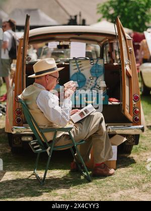 Oldtimer-Besitzer, der sich auf einer Oldtimer-Show in England, Großbritannien, entspannt - Haslemere Classic Car Show Mai 2023 - British Life trinkt Tee Stockfoto