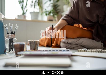 Nahaufnahme Hand der Künstlerin hält Pinselgemälde mit Aquarell im Skizzenbuch im Kunststudio. Stockfoto