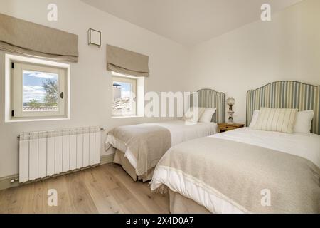 Ein Schlafzimmer mit zwei Einzelbetten, Kopfteilen mit gestreiftem Stoff, passenden Kissen und Kissen und zwei quadratischen Fenstern mit Aussicht Stockfoto