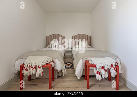 Ein Schlafzimmer mit zwei Einzelbetten, Kopfteilen mit rot gestreiftem Stoff, passenden Kissen und Kissen und einem zentralen Nachttisch aus Holz Stockfoto