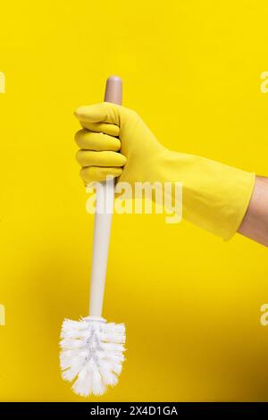 Handgelber Gummihandschuh hält Toilettenbürste gelber Hintergrund Stockfoto