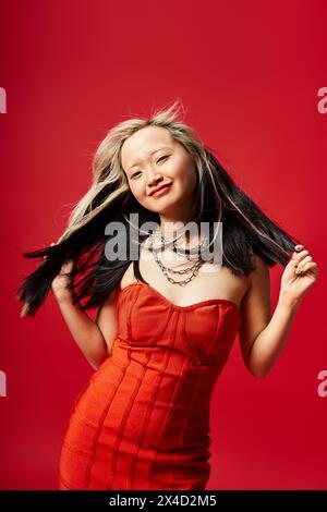 Eine asiatische Frau in einem fließenden roten Kleid posiert anmutig mit ihren langen Haaren. Stockfoto