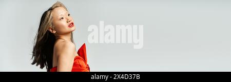 Eine attraktive asiatische Frau posiert selbstbewusst in einem leuchtend roten Kleid. Stockfoto