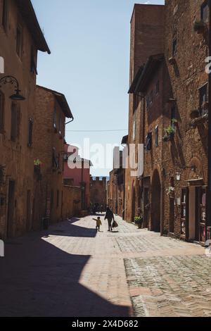 Zwei Leute laufen die Hauptstraße in der Altstadt von Certaldo - Certaldo Alto - in der Toskana, Italien. Aufgenommen an einem sonnigen Apriltag mit hellem Himmel. Stockfoto