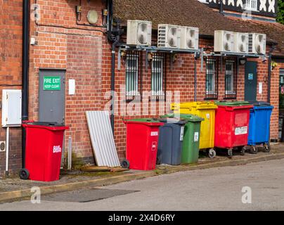 Reihe von farbenfrohen Recycling-Abfallbehältern aus Kunststoff hinter Geschäftsräumen. Stockfoto