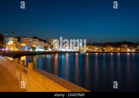 Muttrah Corniche in der Abenddämmerung, Berge in der Ferne, der Persische Golf unterhalb der Stadt. Muttrah, Maskat, Oman. Stockfoto