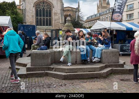 Menschen, die auf Steinsitzen sitzen auf einem geschäftigen Markt mit Zelten und Fußgängern Street Food genießen Stockfoto